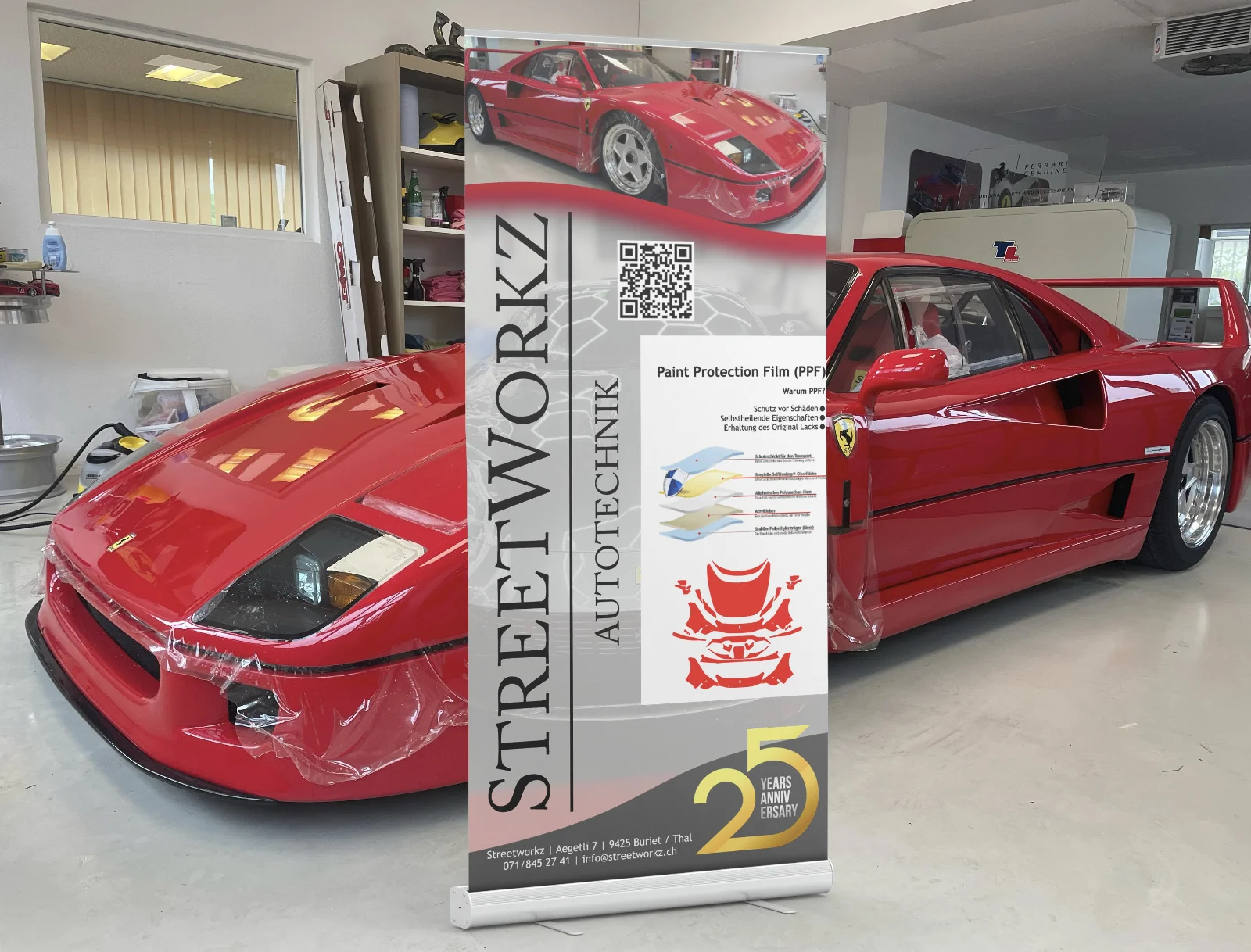 Roter Ferrari in der Werkstatt neben einem Banner für Lackschutzfolie von Streetworkz Autotechnik