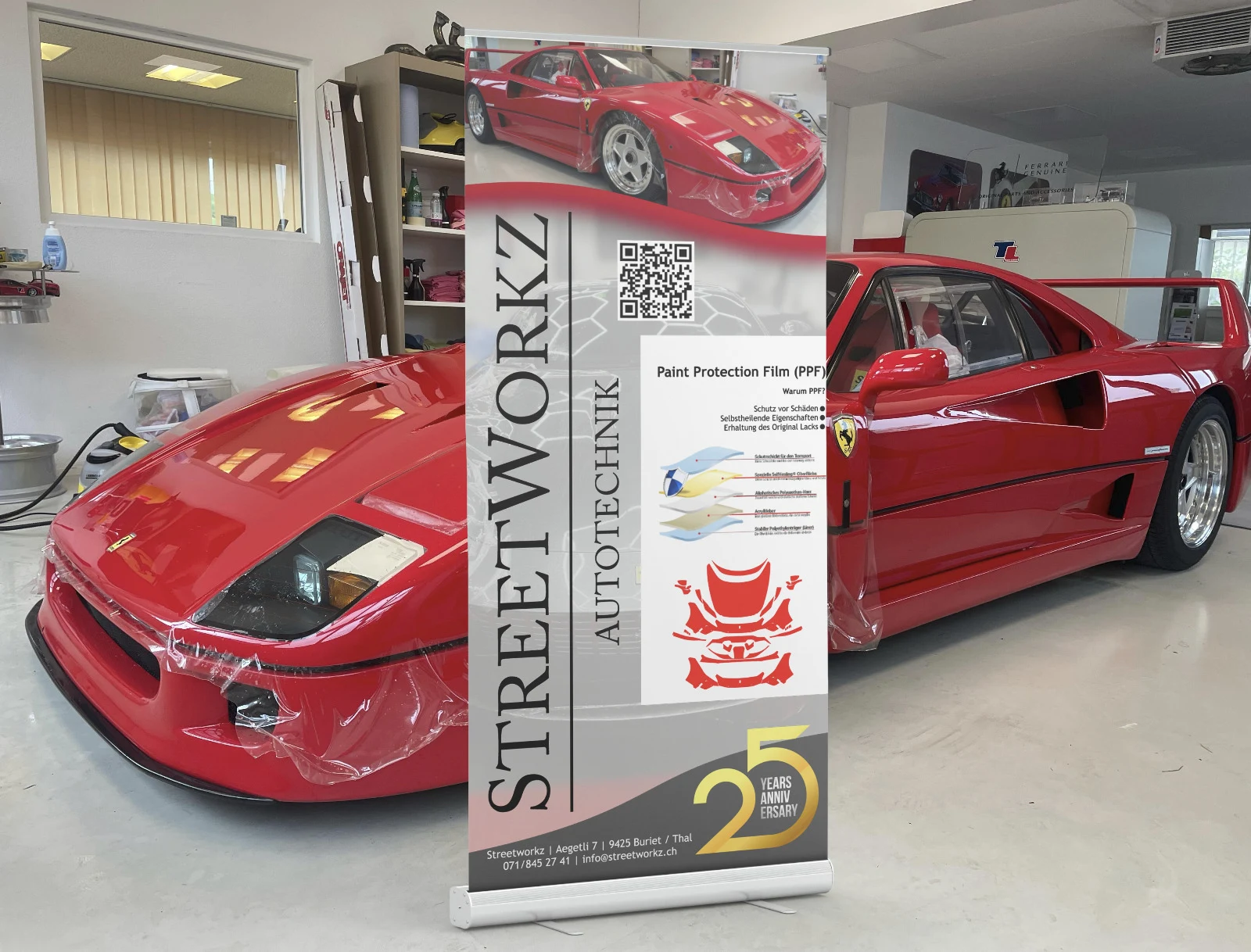 Roter Ferrari in der Werkstatt neben einem Banner für Lackschutzfolie von Streetworkz Autotechnik